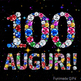 Il numero 100 e l'espressione Auguri disegnati da gioielli brillanti multicolori, circondati da piccole scintille su uno sfondo scuro.