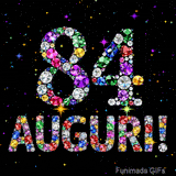 Immagine che mostra il numero 84 e il testo Auguri composti da cristalli luminosi di vari colori su una tela nera piena di stelle animate.