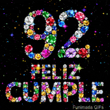 Sobre fondo negro decorado con estrellas y destellos, aparece la cifra 92 y las palabras FELIZ CUMPLE compuestos de diamantes coloridos.