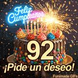 Tarta de celebración mostrando el dígito 92, iluminada por destellos. Estrellitas doradas caen sobre la brillante frase festiva en el frente.