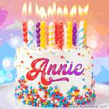 A cheerful white birthday cake with multicolor sprinkles, lit candles, and 'Annie' written in vibrant letters, in an animated GIF.