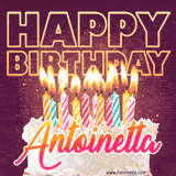 A colorful birthday cake topped with lit candles, with the words 'Happy Birthday Antoinetta' in bold glowing letters on a burgundy background. Animated flames add a festive touch.