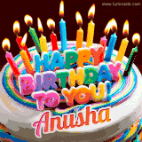 A colorful birthday cake topped with lit candles, with the words 'Happy Birthday Anusha' in bold glowing letters on a burgundy background. Animated flames add a festive touch.