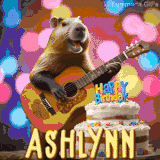 Animated birthday GIF showing a capybara playing guitar and singing beside a birthday cake with the name Ashlynn in large letters and colorful bokeh lights in the background.