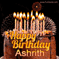 A rich chocolate cake topped with glowing birthday candles and surrounded by bright fireworks. The animated GIF displays the message 'Happy Birthday Ashrith' in golden text.