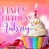 A vibrant birthday GIF featuring a rainbow-colored cupcake topped with white frosting, sprinkles, and a lit candle. The text reads 'Happy Birthday Aubrey' in bold pink and violet letters with white outline.