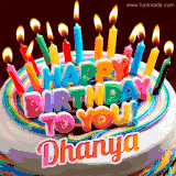 A colorful birthday cake topped with lit candles, with the words 'Happy Birthday Dhanya' in bold glowing letters on a burgundy background. Animated flames add a festive touch.