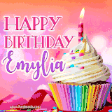 A vibrant birthday GIF featuring a rainbow-colored cupcake topped with white frosting, sprinkles, and a lit candle. The text reads 'Happy Birthday Emylia' in bold pink and violet letters with white outline.