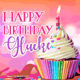 A vibrant birthday GIF featuring a rainbow-colored cupcake topped with white frosting, sprinkles, and a lit candle. The text reads 'Happy Birthday Glucke' in bold pink and violet letters with white outline.