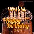 A rich chocolate cake topped with glowing birthday candles and surrounded by bright fireworks. The animated GIF displays the message 'Happy Birthday Jakhi' in golden text.