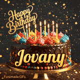 A chocolate drip birthday cake on a stand with colorful frosting and lit candles, featuring the name Jovany in glowing yellow letters.