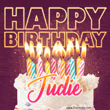 A colorful birthday cake topped with lit candles, with the words 'Happy Birthday Judie' in bold glowing letters on a burgundy background. Animated flames add a festive touch.