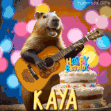 Animated birthday GIF showing a capybara playing guitar and singing beside a birthday cake with the name Kaya in large letters and colorful bokeh lights in the background.