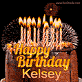A rich chocolate cake topped with glowing birthday candles and surrounded by bright fireworks. The animated GIF displays the message 'Happy Birthday Kelsey' in golden text.
