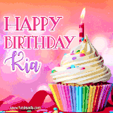 A vibrant birthday GIF featuring a rainbow-colored cupcake topped with white frosting, sprinkles, and a lit candle. The text reads 'Happy Birthday Kia' in bold pink and violet letters with white outline.