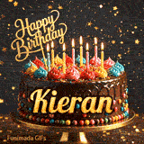 Close-up of a chocolate birthday cake with multi-colored frosting swirls, lit candles, and a glittering gold Happy Birthday sign. Kieran