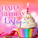 A vibrant birthday GIF featuring a rainbow-colored cupcake topped with white frosting, sprinkles, and a lit candle. The text reads 'Happy Birthday Lesley' in bold pink and violet letters with white outline.
