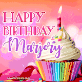 A vibrant birthday GIF featuring a rainbow-colored cupcake topped with white frosting, sprinkles, and a lit candle. The text reads 'Happy Birthday Marjory' in bold pink and violet letters with white outline.