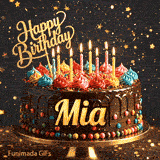 Gold Happy Birthday topper and bright burning candles on a chocolate frosted cake with the name Mia.