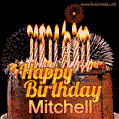 A rich chocolate cake topped with glowing birthday candles and surrounded by bright fireworks. The animated GIF displays the message 'Happy Birthday Mitchell' in golden text.