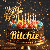 A chocolate frosted birthday cake on a gold stand with lit candles and the name Ritchie in bold yellow letters.