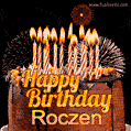 A rich chocolate cake topped with glowing birthday candles and surrounded by bright fireworks. The animated GIF displays the message 'Happy Birthday Roczen' in golden text.