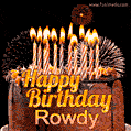 A rich chocolate cake topped with glowing birthday candles and surrounded by bright fireworks. The animated GIF displays the message 'Happy Birthday Rowdy' in golden text.