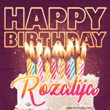 A colorful birthday cake topped with lit candles, with the words 'Happy Birthday Rozalija' in bold glowing letters on a burgundy background. Animated flames add a festive touch.