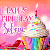 A vibrant birthday GIF featuring a rainbow-colored cupcake topped with white frosting, sprinkles, and a lit candle. The text reads 'Happy Birthday Silvia' in bold pink and violet letters with white outline.