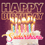 A colorful birthday cake topped with lit candles, with the words 'Happy Birthday Sudarshana' in bold glowing letters on a burgundy background. Animated flames add a festive touch.