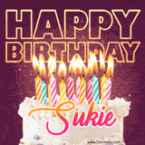 A colorful birthday cake topped with lit candles, with the words 'Happy Birthday Sukie' in bold glowing letters on a burgundy background. Animated flames add a festive touch.