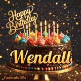 Close-up of a chocolate birthday cake with multi-colored frosting swirls, lit candles, and a glittering gold Happy Birthday sign with name Wendall