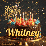 A chocolate frosted birthday cake on a gold stand with lit candles and the name Whitney in bold yellow letters.