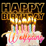 A vibrant animated GIF featuring a delicious birthday cake topped with glowing candles and the name 'Wolfgang' in elegant script, and the words 'Happy Birthday' on the black background.