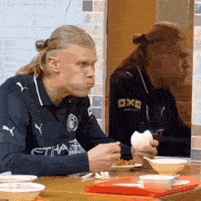 A funny clip showing Erling Haaland eating a meal. He looks to his left into a mirror and suddenly jumps back with a scared, shocked expression when he sees himself in the glass.