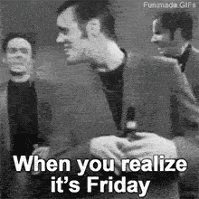 A man in a suit suddenly breaks into a wide, joyful smile in this black and white animated GIF. The on-screen text perfectly captures the moment: 'When you realize it's Friday'.